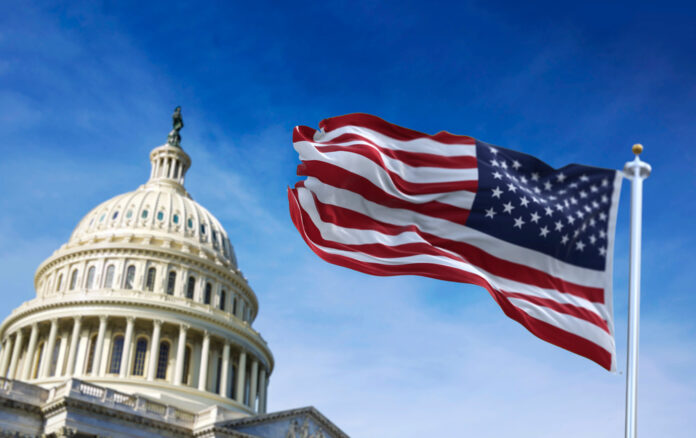 American,Flag,Waving,With,The,Us,Capitol,Hill,In,The